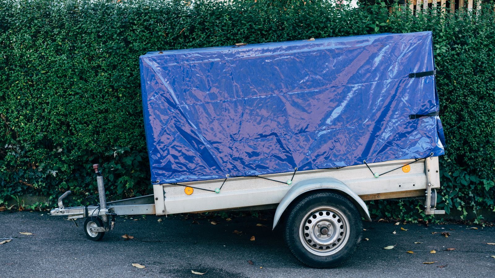 PKW-Anhänger mit blauer Plane am Straßenrand